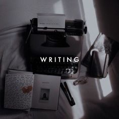 an old typewriter sitting on top of a bed next to a book and pen