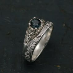 a silver ring with a blue stone in the center on a black surface and an intricate design around it