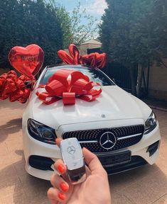 a person holding a cell phone in front of a white car with red bows on it