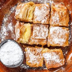 pastries and powdered sugar sit on a plate with a bowl of dipping sauce