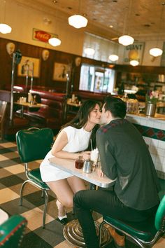 a man and woman sitting at a table in a diner kissing each other's foreheads