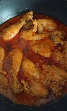 some chicken is cooking in a pan with red sauce on the bottom and meat inside