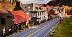 a street lined with small buildings next to a lush green hillside covered in fall leaves