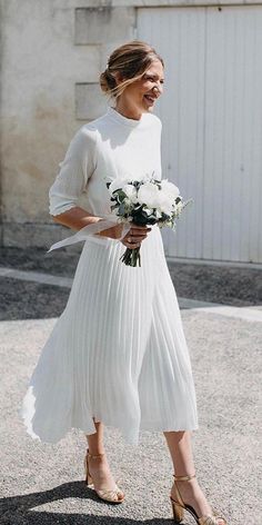 a woman is walking down the street wearing a white dress with pleated skirt and heels