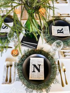 the table is set with black plates, silverware and greenery as centerpieces