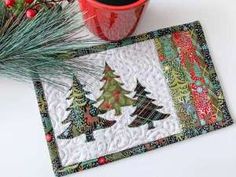 two christmas trees on a placemat next to a potted plant and red mug