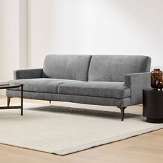 a gray couch sitting on top of a white rug next to a black coffee table