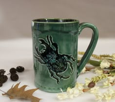 a green coffee mug sitting on top of a table next to dried flowers and leaves