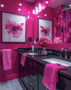 a bathroom decorated in pink and black with flowers on the counter top, two framed pictures above the sink