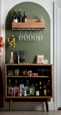 a bar with wine glasses and liquor bottles on the top shelf, next to a vase filled with flowers