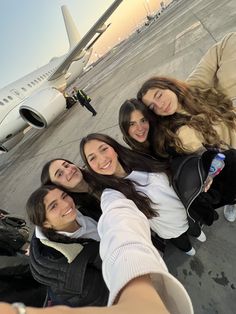 a group of friends taking a selfie in front of an airplane