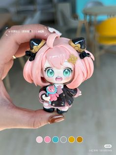 a hand holding a small doll with pink hair and blue eyes in front of a table