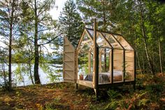 a small house made out of wood and glass in the middle of some grass with trees around it