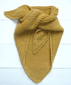 a yellow knitted scarf with a knot on the front and back ends, laying on a white wood floor