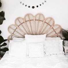 a white bed with wicker headboard and pillows in a room filled with plants