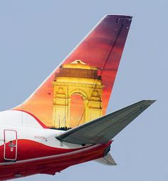 the tail end of an airplane as it flies in the sky with a clock tower on top