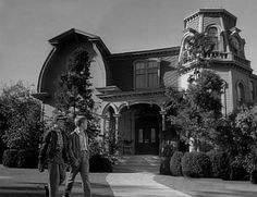 two men walking in front of a large house