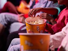 people are sitting in chairs and watching something on the table while one person is holding a bucket full of popcorn