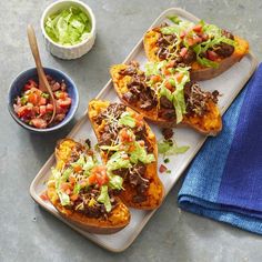 four stuffed sweet potatoes topped with meat, lettuce and tomato salad next to a bowl of salsa