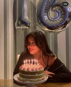 a woman sitting in front of a cake with lit candles on it and balloons behind her