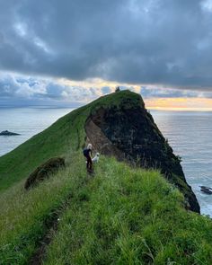 a person walking up the side of a hill next to the ocean on a cloudy day