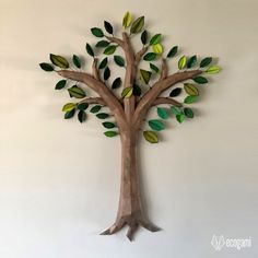 a wooden tree with green leaves hanging on the wall in front of a white wall