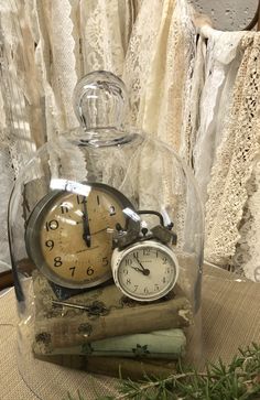 there is a clock under a glass dome on top of books and laces in the background