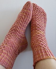 someone wearing pink knitted socks with their feet propped up against the wall and holding on to them