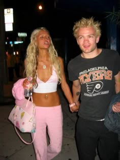 a man and woman holding hands while walking down the street at night with no shirt on