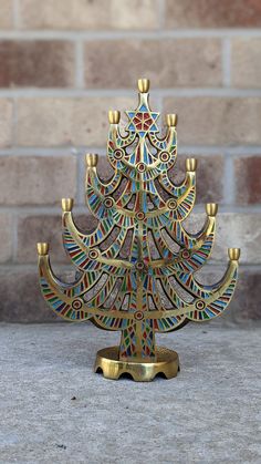 a small multicolored wooden christmas tree with candles on it's stand in front of a brick wall