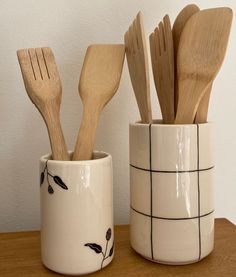 three wooden spoons and two ceramic cups with utensils in them on a table