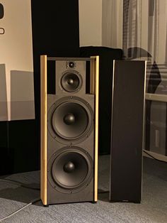 two speakers sitting next to each other in front of a wall mounted speaker system on the floor