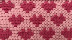 a crocheted blanket with pink and white designs on the bottom, along with red hearts