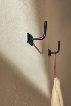 a towel hanging on the wall next to a coat rack with two black hooks in it