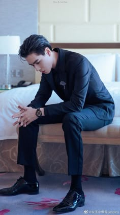 a man sitting on top of a bed next to a white pillow and wearing black shoes