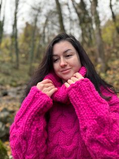 a woman with long hair wearing a pink sweater and posing for a photo in the woods