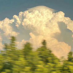 an image of clouds and trees taken from the window of a moving train or bus