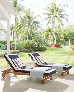 two chaise lounge chairs with towels on them in front of palm trees and lawn