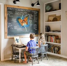 two children sitting at a table in front of a chalkboard