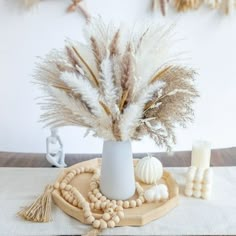 a white vase filled with lots of feathers on top of a wooden table next to candles and beads