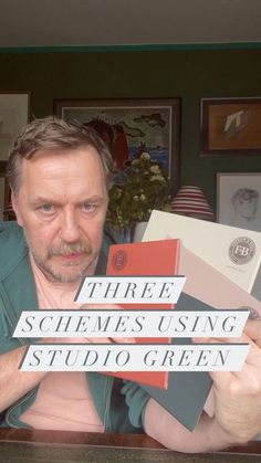 a man sitting at a table holding up some type of sign that says three schemes using studio green