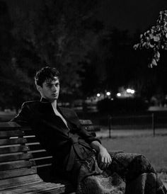 black and white photograph of a man sitting on a park bench in the night time