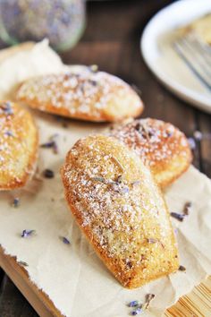 three pastries on a piece of paper with lavender sprinkled on them and two plates in the background