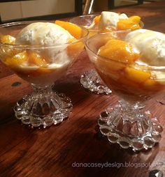 two glasses filled with ice cream and fruit on top of a wooden table next to each other