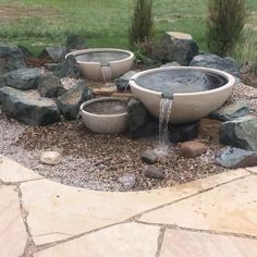 an outdoor fountain with two bowls and water coming out of the top, surrounded by rocks