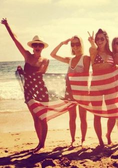 three women in bathing suits holding an american flag on the beach while standing next to each other