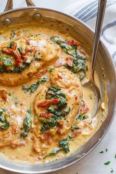 chicken with spinach and tomato sauce in a silver skillet on a white table