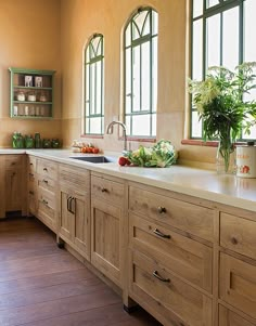 a large kitchen with wooden cabinets and white counter tops, along with two potted plants on the window sill