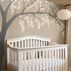 a baby's room with a tree painted on the wall and white crib