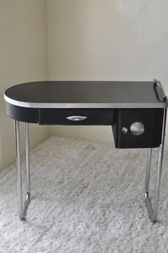 a black desk with two drawers on top of white carpeted floor next to wall